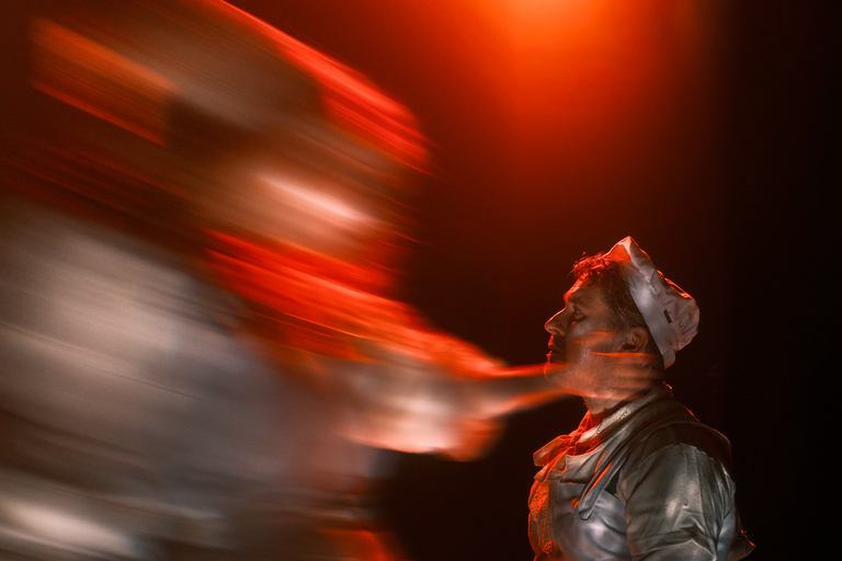 Dramatic theatrical stage performance from Into the Woods musical with red lighting and motion blur over actor wearing a white bonnet and costume.